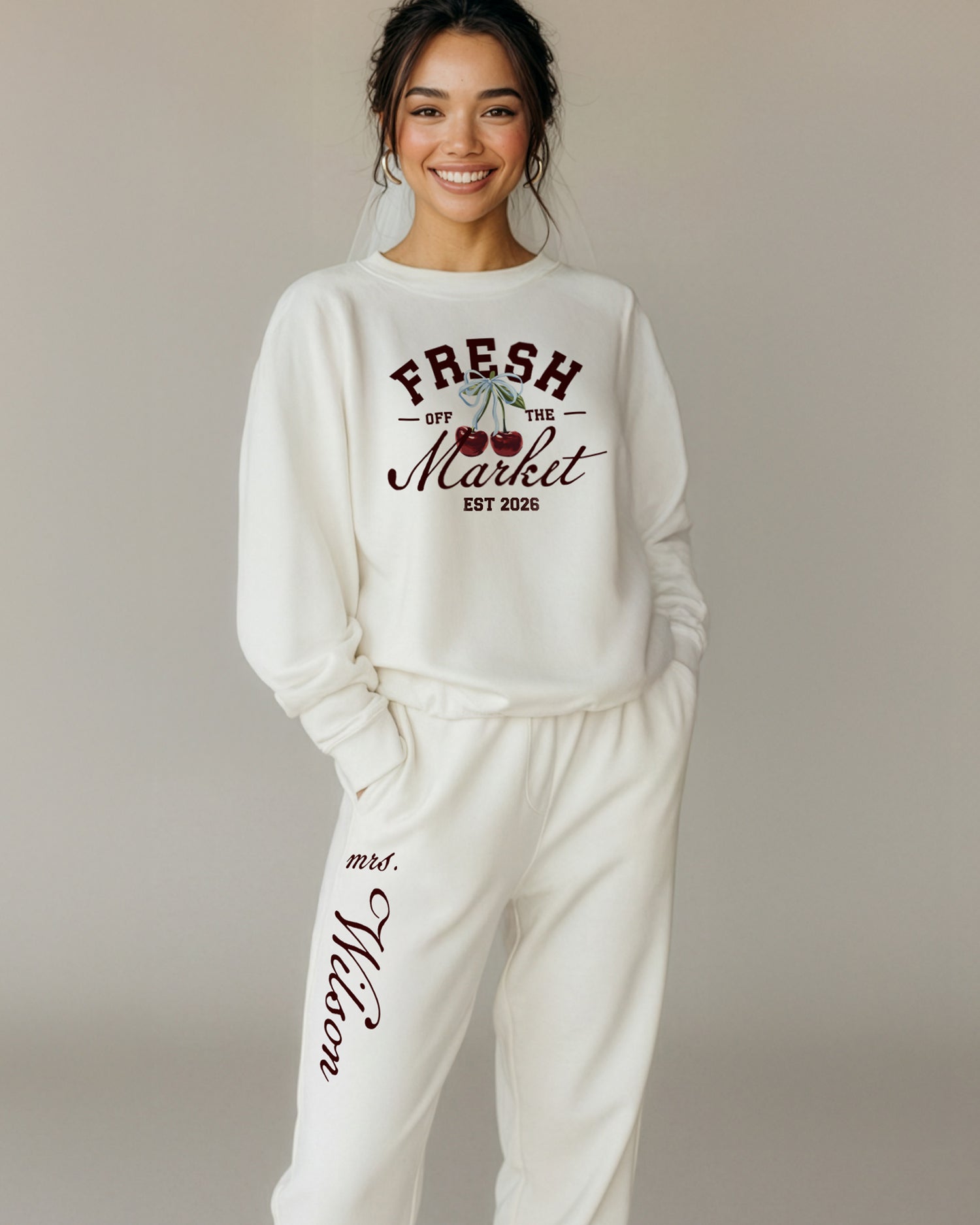 Woman wearing a white sweatshirt and pants with print that reads "Fresh Off The Market." Bride Loungewear