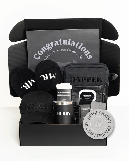 Groomsmen gift set with hats, mug, and other items in a black box labeled 'Congratulations Welcome to the Groom Life'.