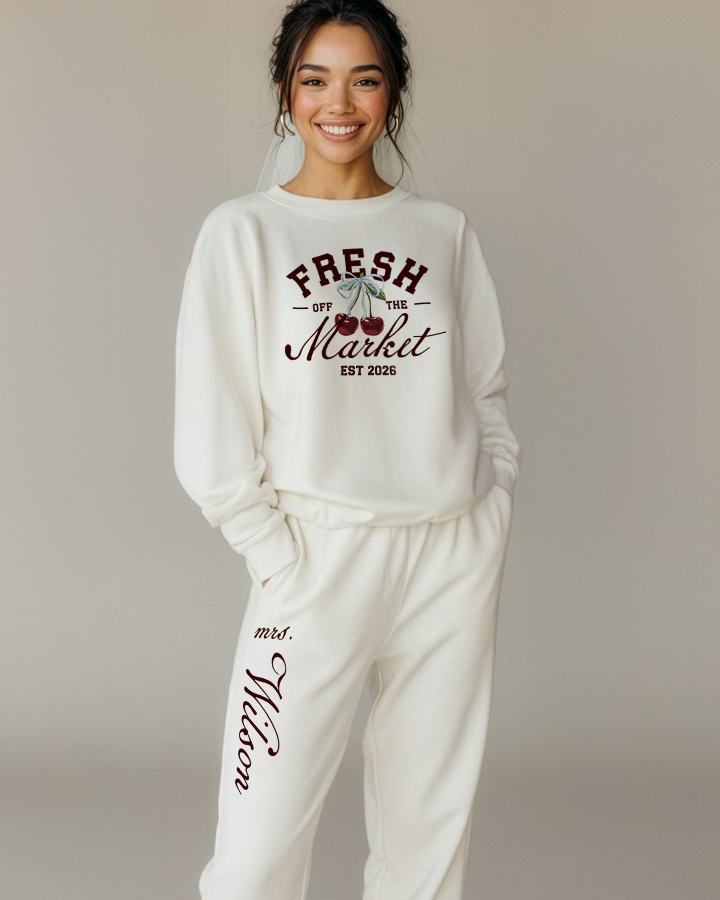 Woman wearing a white sweatshirt and pants with print that reads "Fresh Off The Market." Bride Loungewear