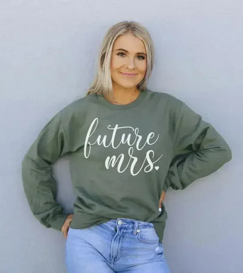 Woman wearing a green sweatshirt with 'future mrs.' text against a plain background