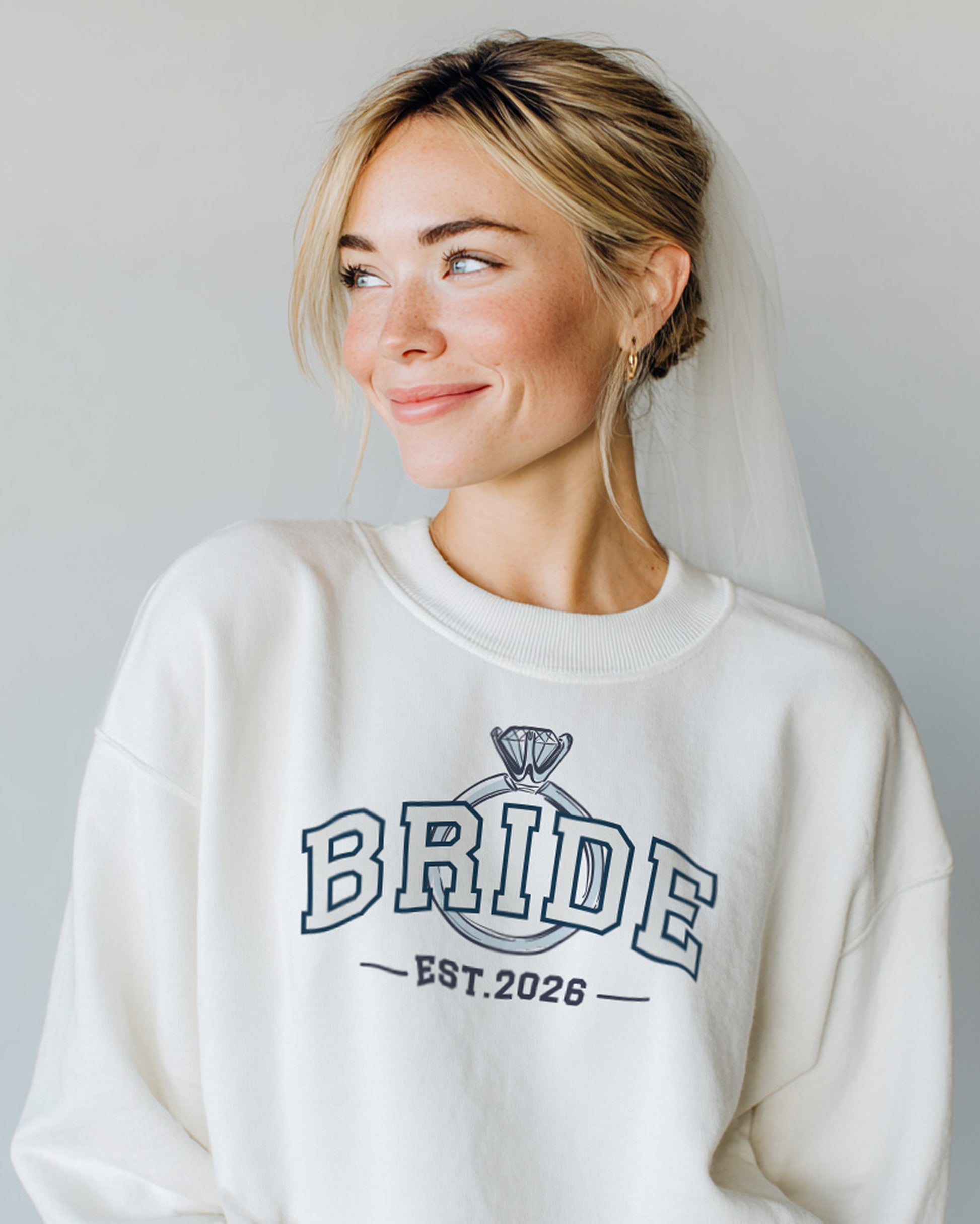 Woman wearing a white sweatshirt with 'BRIDE EST. 2026' and engagement ring print. Bride sweatshirt