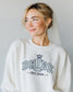 Woman wearing a white sweatshirt with 'BRIDE EST. 2026' and engagement ring print. Bride sweatshirt