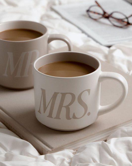 Two ceramic coffee mugs filled with coffee, one printed with 'MR.' and the other with 'MRS.