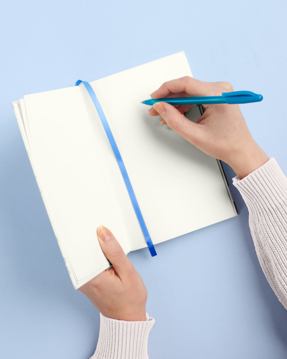 Person writing in a notebook with a blue pen on a light blue background